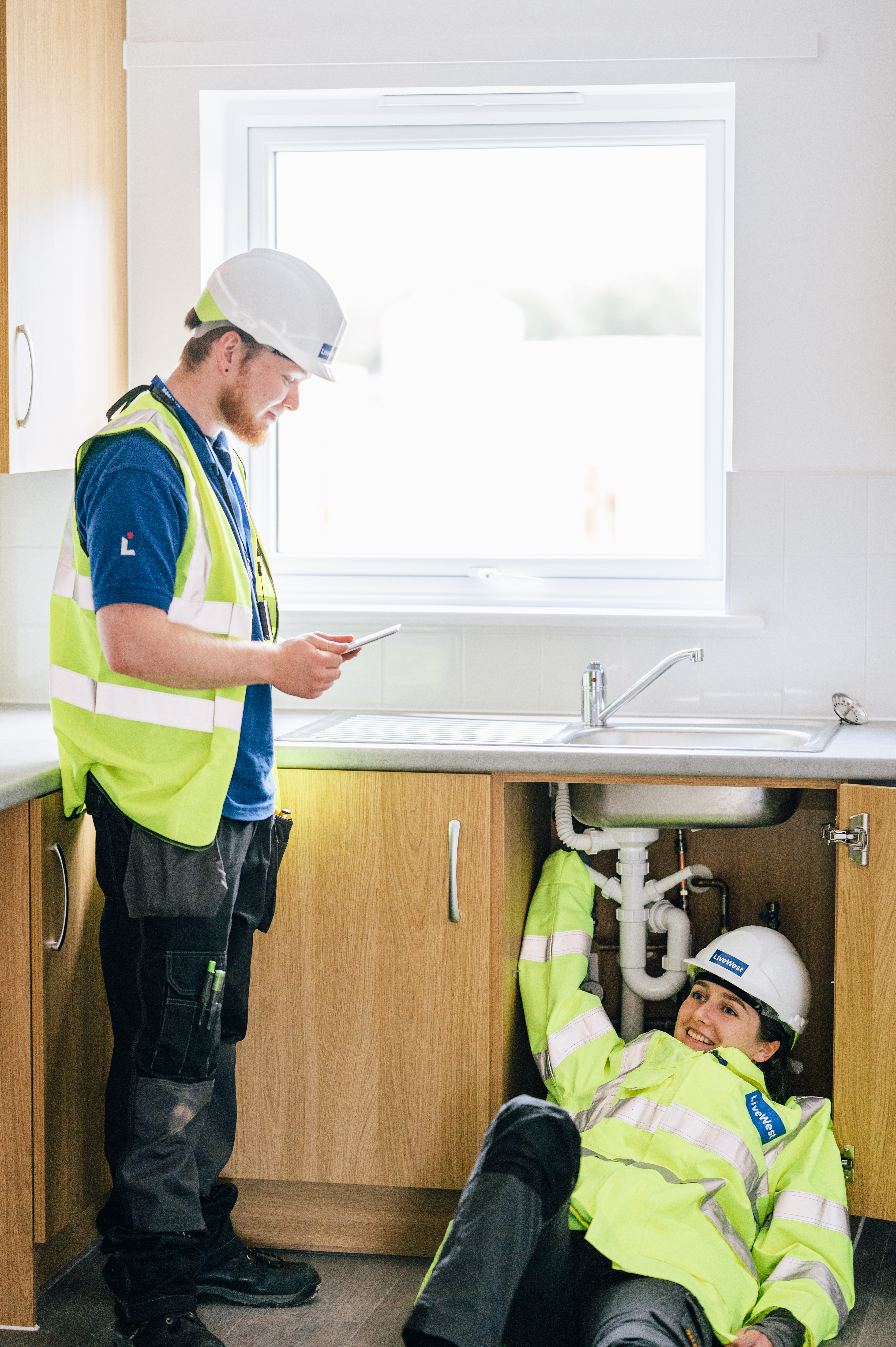 Male and female trades colleagues working underneath a customer's sink
