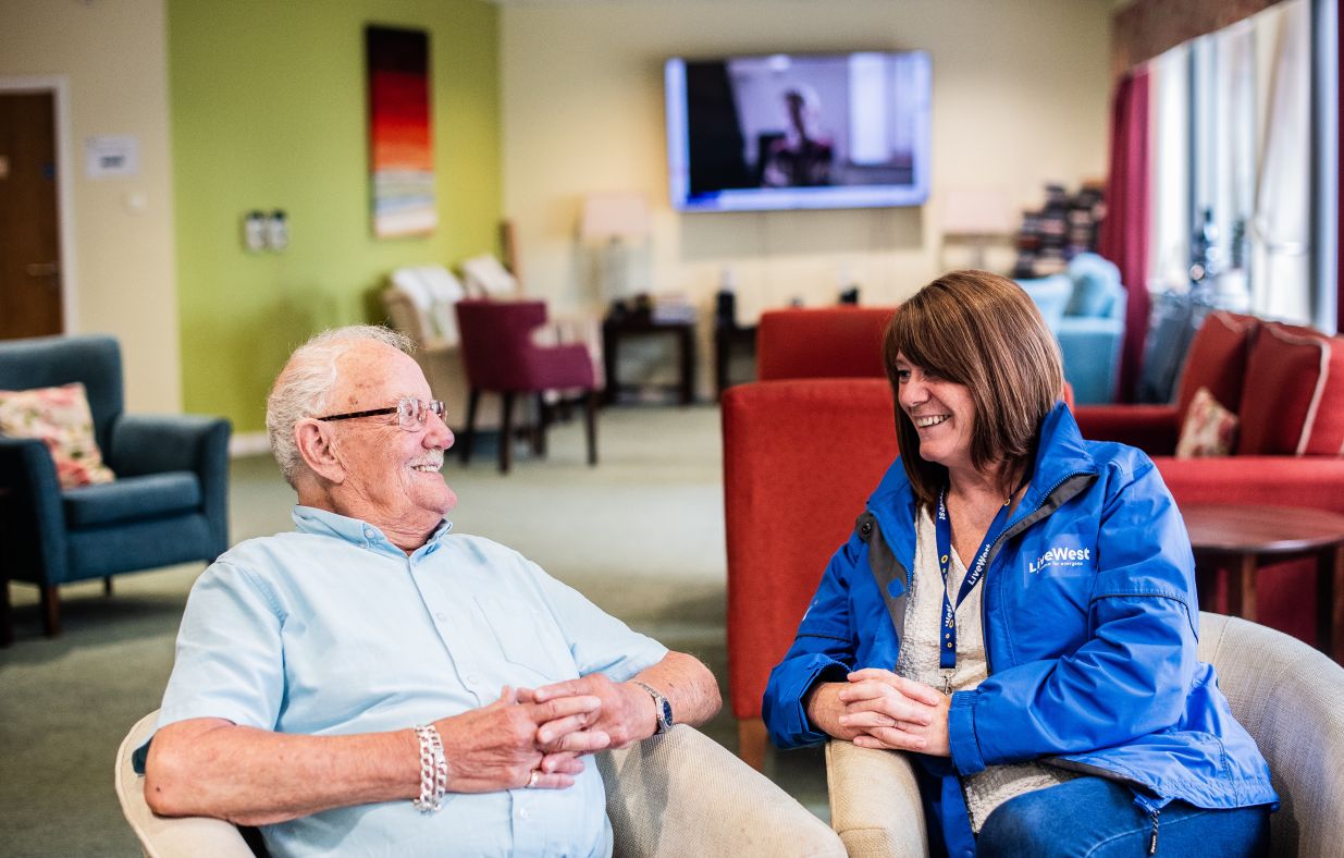 A LiveWest colleague sitting alongside a resident in Devonport Views' communal area.