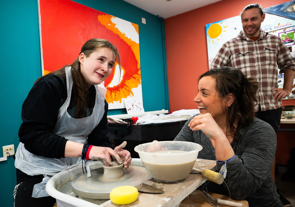 Three people are enjoying making pottery together in a bright and colourful room.