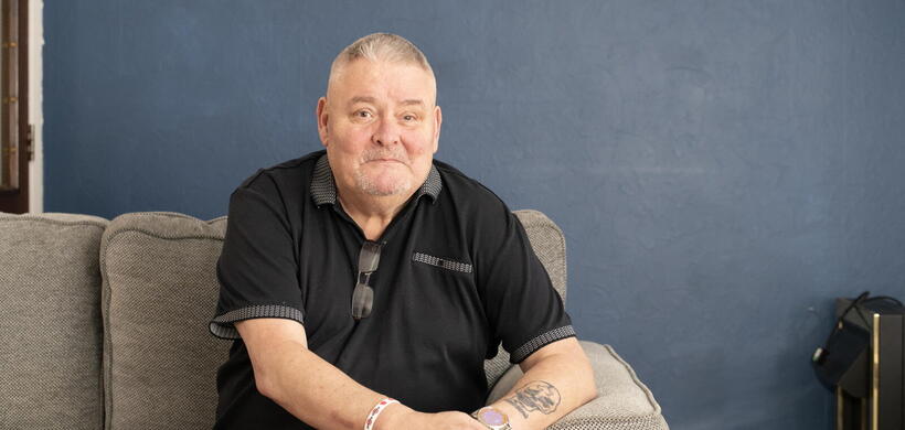 An image of Mark, a military veteran and LiveWest resident, smiling at the camera on the sofa.