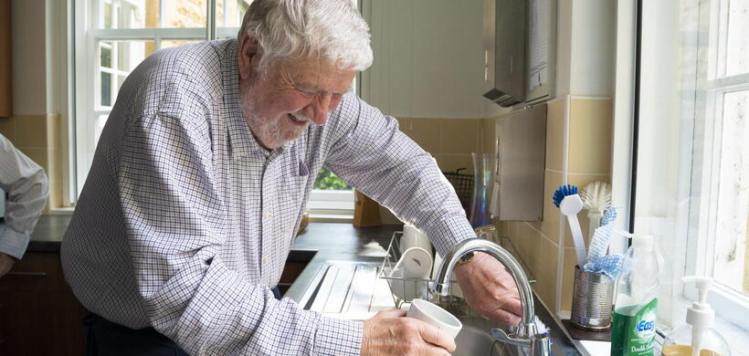 A man is filling a cup with water from a kitchen tap in a well-lit room.