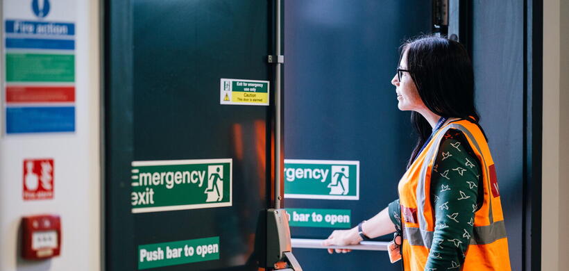 A person wearing a safety vest is opening an emergency exit door in a building.