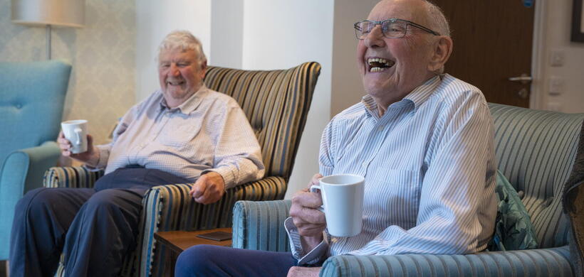 Older customers enjoying a cup of coffee and laughing at a extra care supported housing scheme.