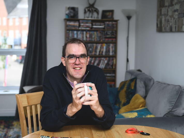 Iain sat at his table drinking a hot drink in his new flat.