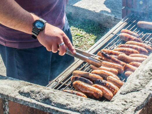 A man is cooking sausages on a barbecue at an outdoor event.