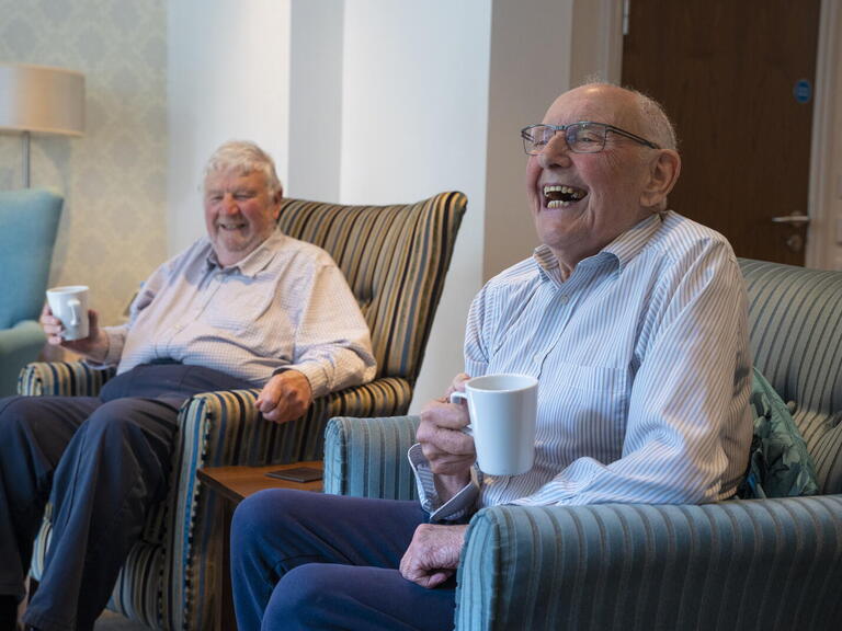 Older customers enjoying a cup of coffee and laughing at a extra care supported housing scheme.