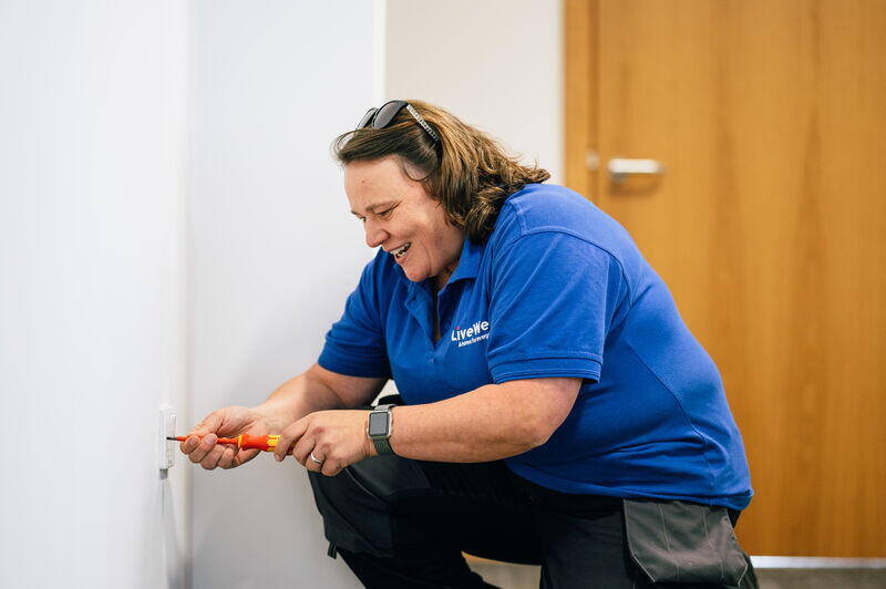 Image shows apprentice, Claire, working on a plug socket and smiling whilst wearing LiveWest uniform