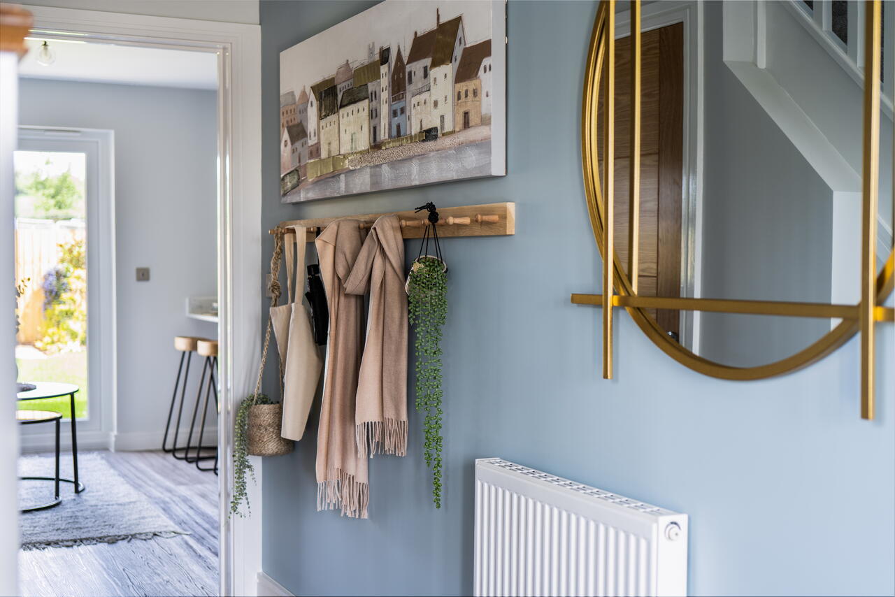 Image shows a hallway in a home decorated with a mirror, coat hooks and artwork.