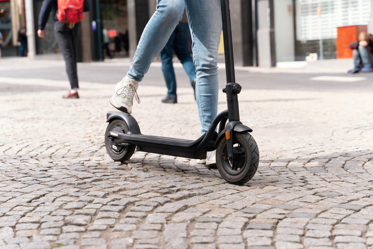 Image shows a person riding an e-scooter on a cobbled road.