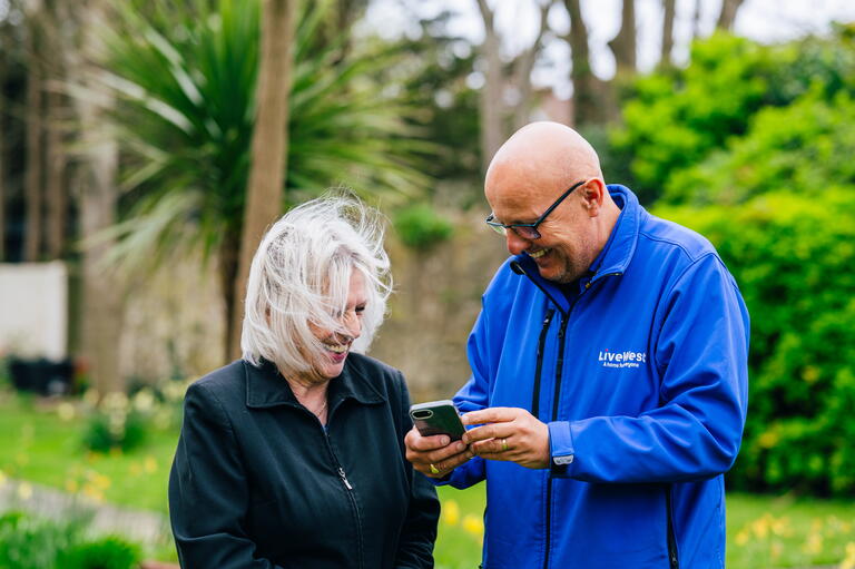 A LiveWest colleague is showing a customer a phone screen and smiling together.