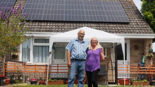 Malcolm and Michelle standing outside of their home with solar panels