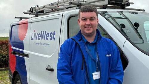 Image shows Apprentice, Alex, stood smiling in front of a LiveWest van