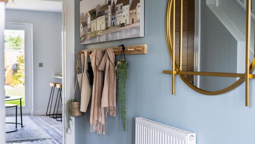 Image shows a hallway in a home decorated with a mirror, coat hooks and artwork.