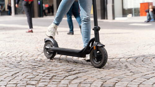 Image shows a person riding an e-scooter on a cobbled road.