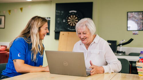 Image shows a LiveWest colleague and customer sat at a table looking at a laptop.