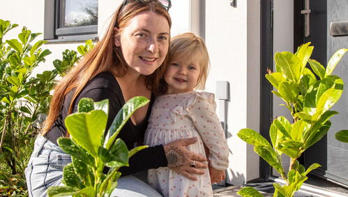 A woman and her daughter are smiling in front of their home.