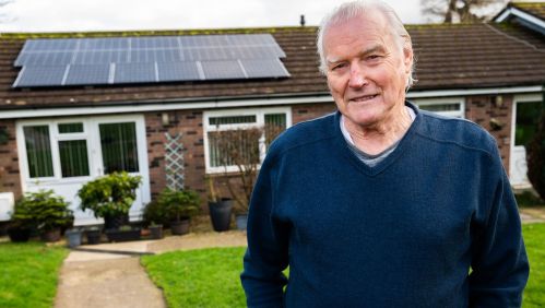 Patrick smiling outside his home with new solar panels.